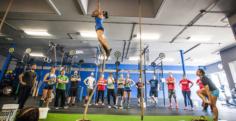 a woman climbing a rope with the rest of the gym members cheering her own 